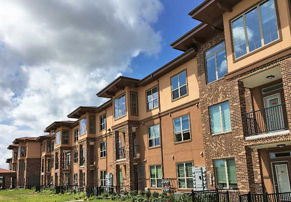A row of brown brick apartment buildings with green shutters and balconies.