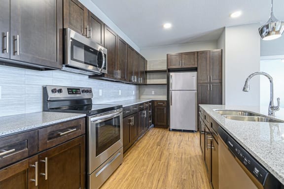 a kitchen with wooden cabinets and stainless steel appliances at The Fitzroy San Marcos, San Marcos, TX