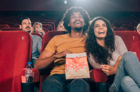 a group of people sitting in a movie theater laughing and holding popcorn