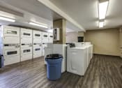 Thumbnail 19 of 27 - A laundry room with a washer and dryer, a trash can, and a table.