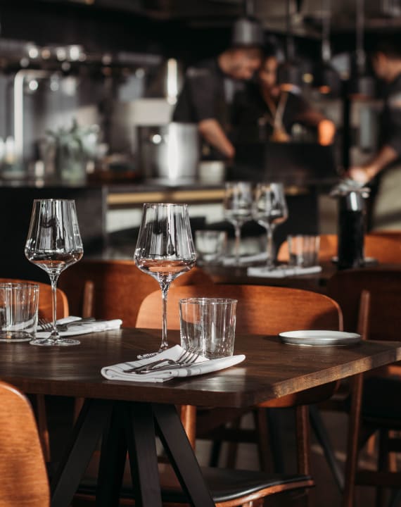A restaurant with wooden tables and chairs and a chef in the background.