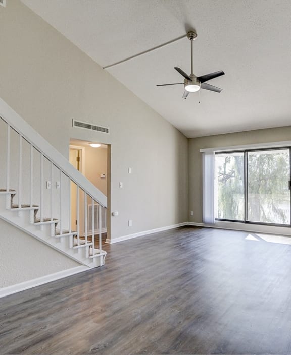 an empty living room with a staircase and a ceiling fan