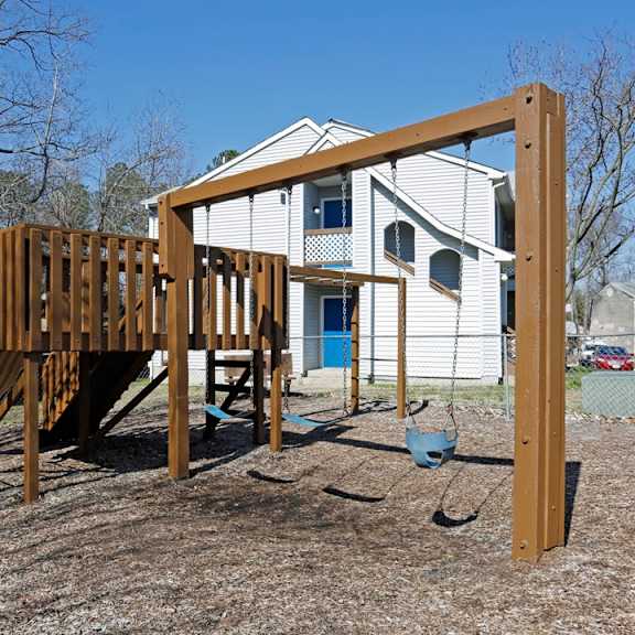 A wooden swing set in front of a white house.