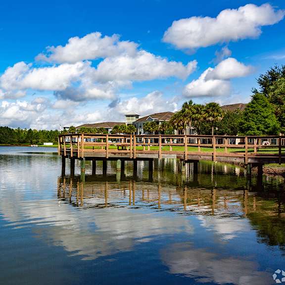 A wooden pier extends into a calm body of water under a blue sky with scattered clouds.