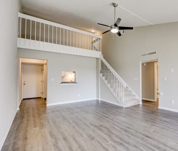 an empty living room with a staircase and a ceiling fan
