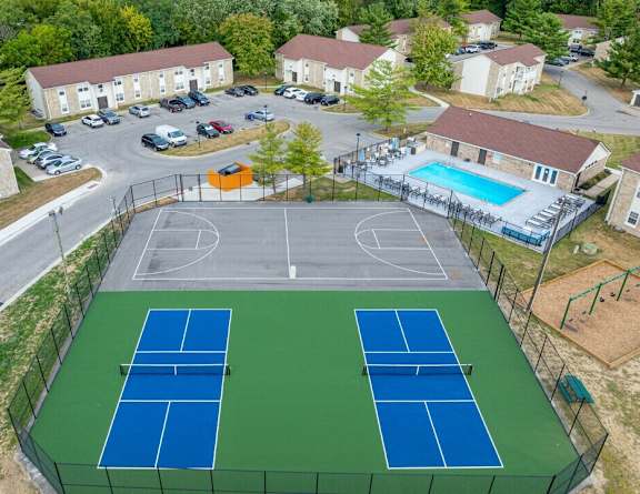 A tennis court is surrounded by a fence and a basketball court is in the background.