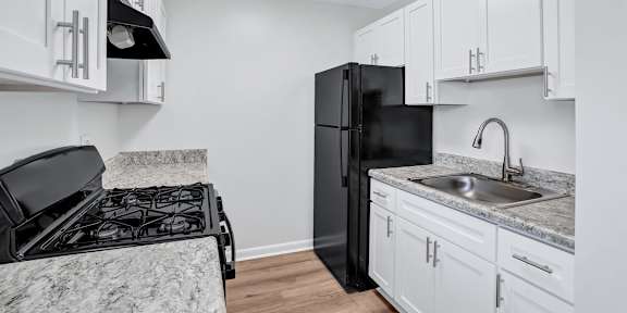 A black refrigerator sits in a kitchen with white cabinets.