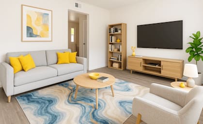 A living room with a grey couch, a wooden coffee table, a white armchair, a blue rug, a wooden bookshelf, a flat screen TV, and a plant.