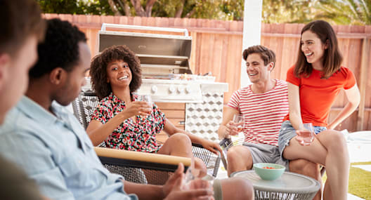 a group of people sitting around a backyard patio talking and drinking wine
