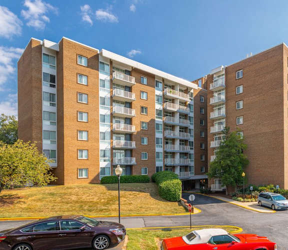 A red car is parked in a parking lot in front of a brick apartment building. at Charlestowne North Apartments, Maryland