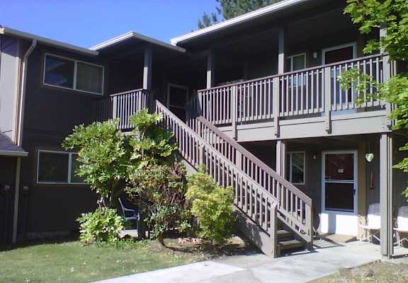 A brown house with a deck and stairs leading to the front door.