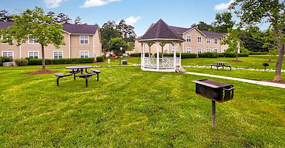 a gazebo and picnic tables in a grassy area with apartment buildings in the