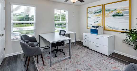 A room with a desk, chairs, and a ceiling fan.