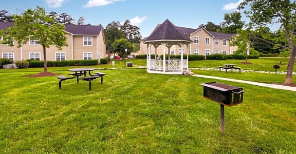 a gazebo and picnic tables in a grassy area with apartment buildings in the