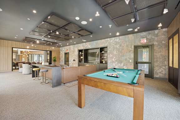 A billiard table with a green cloth is in the center of a room with a stone wall and a ceiling with lights.