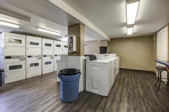 A laundry room with a washer and dryer, a trash can, and a table.