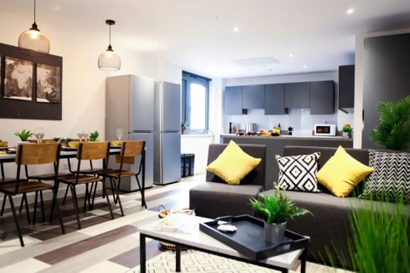 a kitchen and living room with a grey couch and yellow pillows