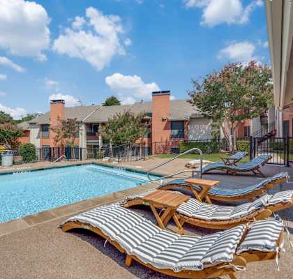 A pool surrounded by lounge chairs and a fence. at Infinity on the Oaks Apartments, Dallas, TX