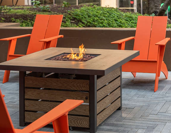 a patio with a fire table and orange chairs