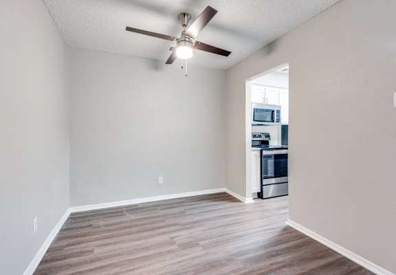 A room with a ceiling fan and a kitchen in the background at Infinity on the Oaks Apartments, Dallas, TX