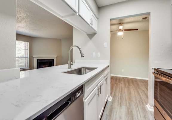 A kitchen with a white counter top and a stainless steel dishwasher at Infinity on the Oaks Apartments, Dallas, TX