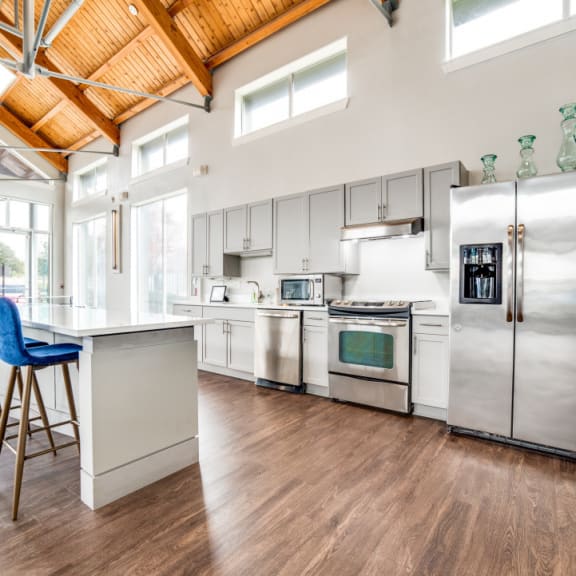 a kitchen with stainless steel appliances and a bar with blue chairs at The Landings at Brooks City-Base, San Antonio, TX, 78235