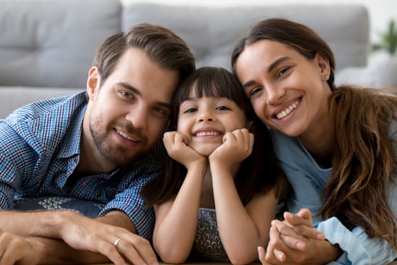 A family of three is sitting closely together on a couch.