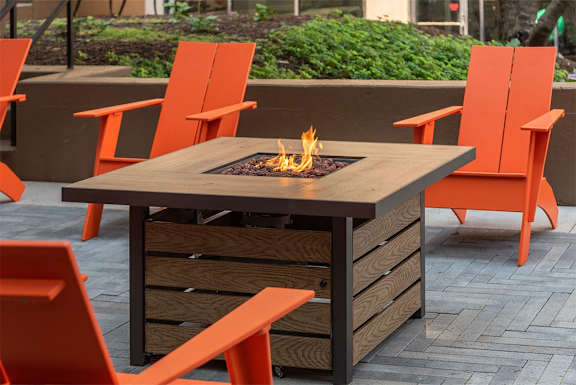 a patio with a fire table and orange chairs