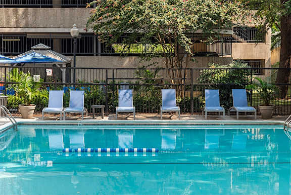 a swimming pool with blue lounge chairs and a building in the background