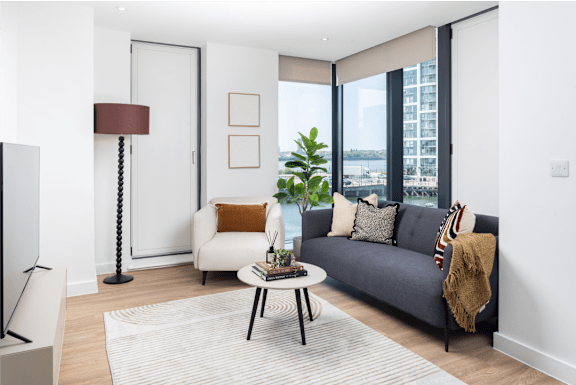 A living room with a grey couch, a coffee table, a lamp, and a plant.