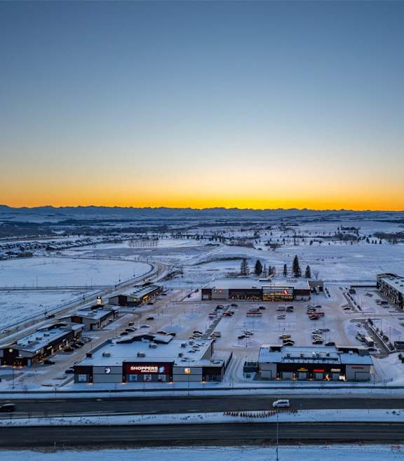 A sunset view of a snowy parking lot with several buildings.