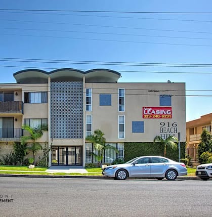 A modern apartment building with a leasing sign in front.