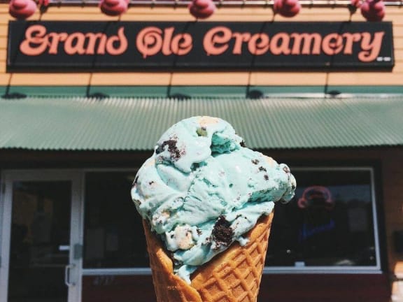 a cone of mint and chocolate ice cream in front of an ice cream shop