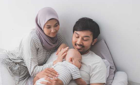 a man and woman sitting on a bed holding a baby