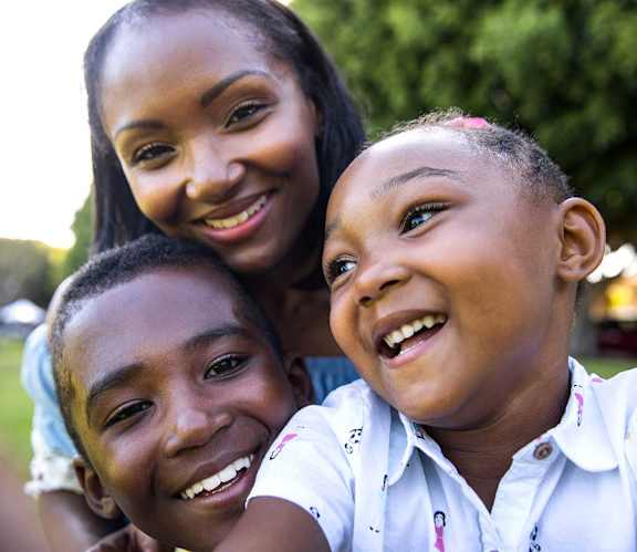 A woman and two children are smiling and enjoying each other's company in a park.