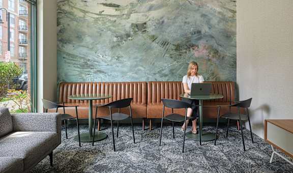 A woman is sitting at a table in front of a large painting.