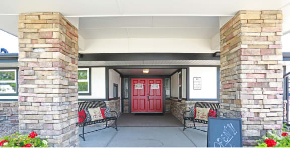 a red door on a building with a porch with two benches and a chalkboard sign