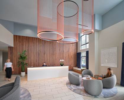 A reception area with a white reception desk and a woman sitting on a grey chair.