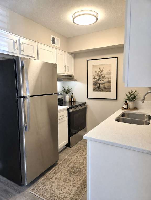 A kitchen with a refrigerator, sink, and cabinets.