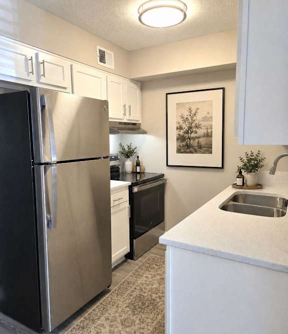 A kitchen with a refrigerator, sink, and cabinets.