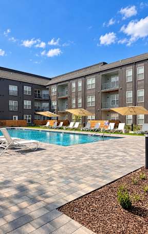 A pool surrounded by chairs and umbrellas outside a building.