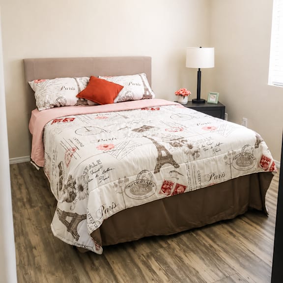 A bed with a white comforter and a pink pillowcase is in a room with a lamp and a picture frame on a nightstand.