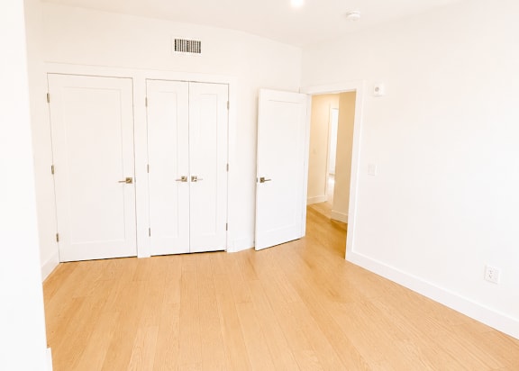 A room with white walls and wooden flooring with three white doors.