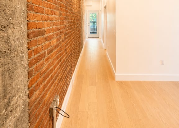A long hallway with a brick wall on the left and wooden floors.