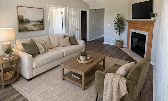A living room with a white couch, a green armchair, a wooden coffee table, and a fireplace with a TV above it.