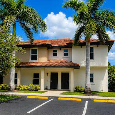 A two-story house with a red tile roof and a palm tree in front.