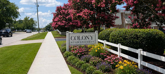 A white fence with a sign that says Colony in front of a flowering tree.