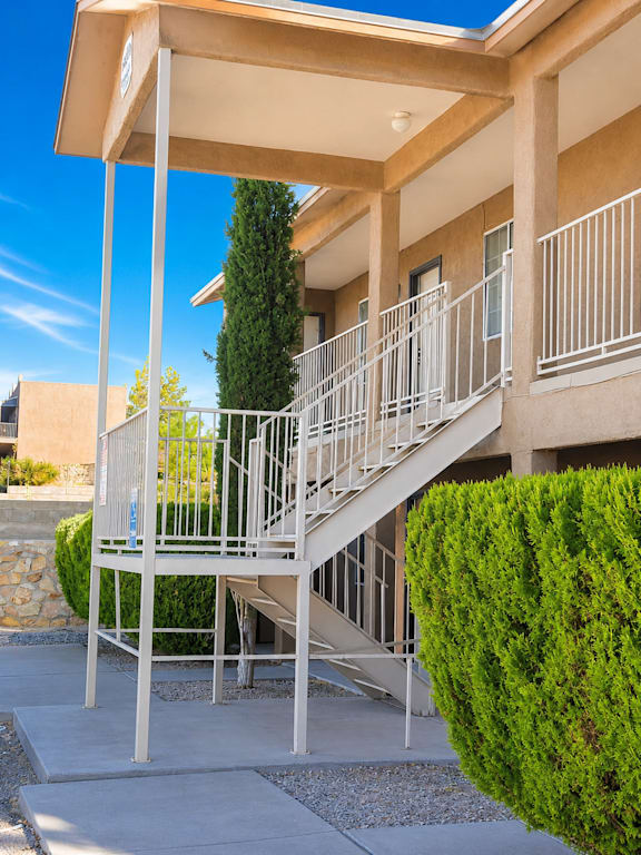 A staircase with a metal railing and a green bush on the side.