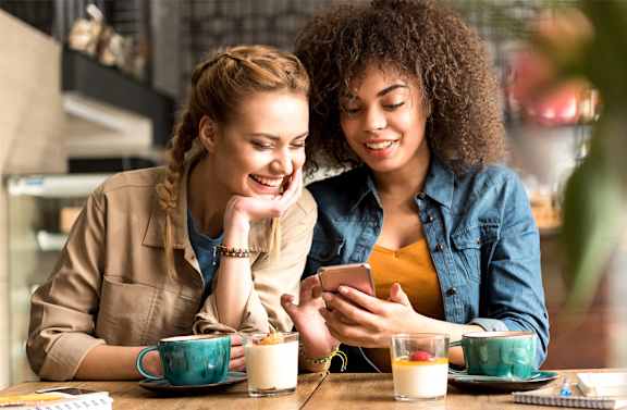 Two women are sitting at a table with drinks and a smartphone.