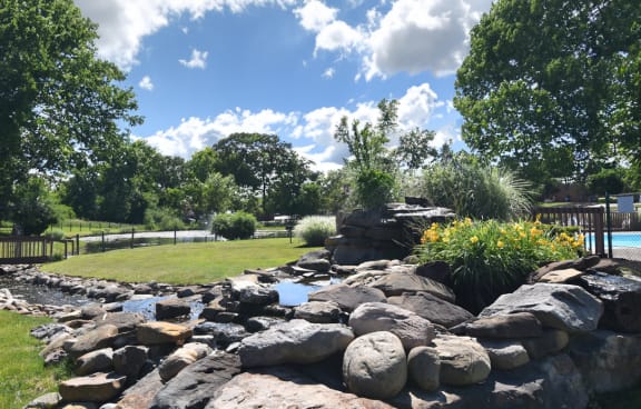 a rock waterfall in a park with a pond and trees